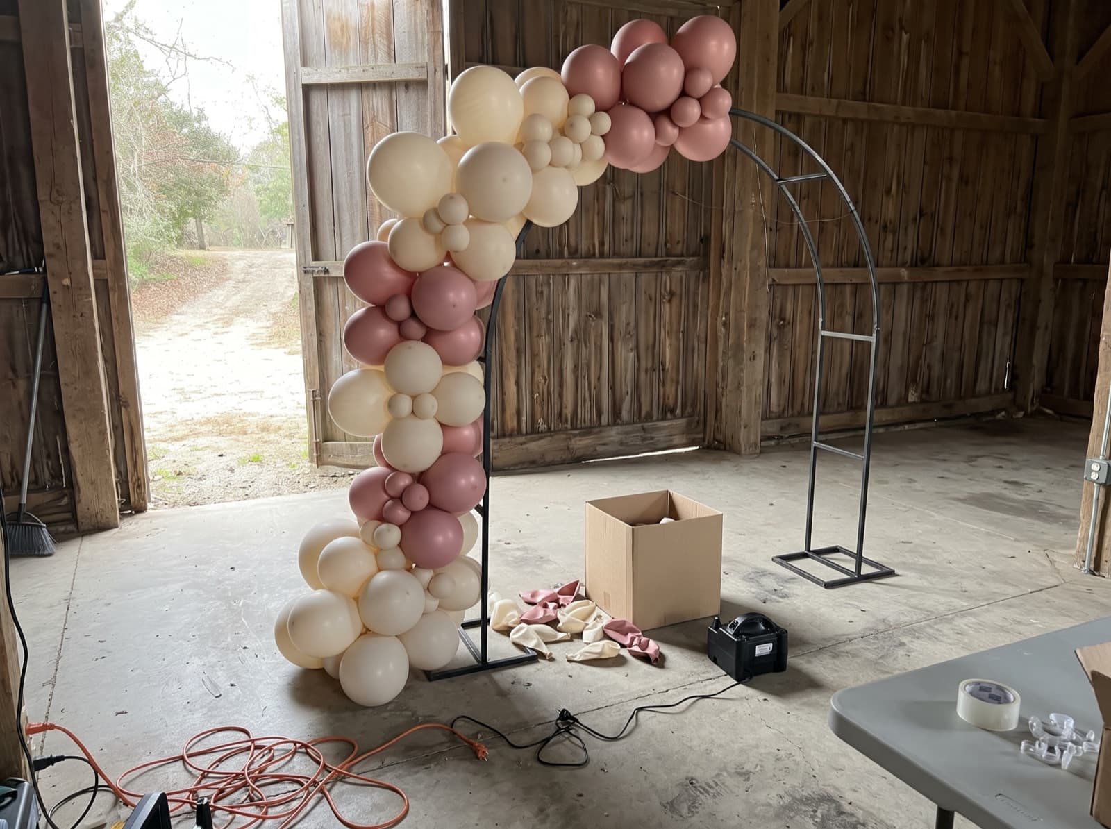 Organic balloon garland half-built on an arch frame in an empty event barn before a party