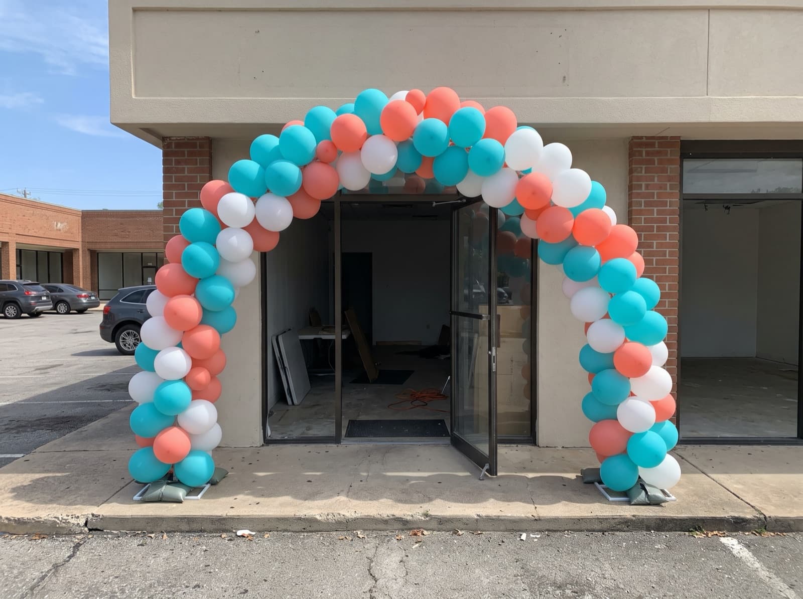 Large balloon arch in turquoise, coral and white over a shop entrance