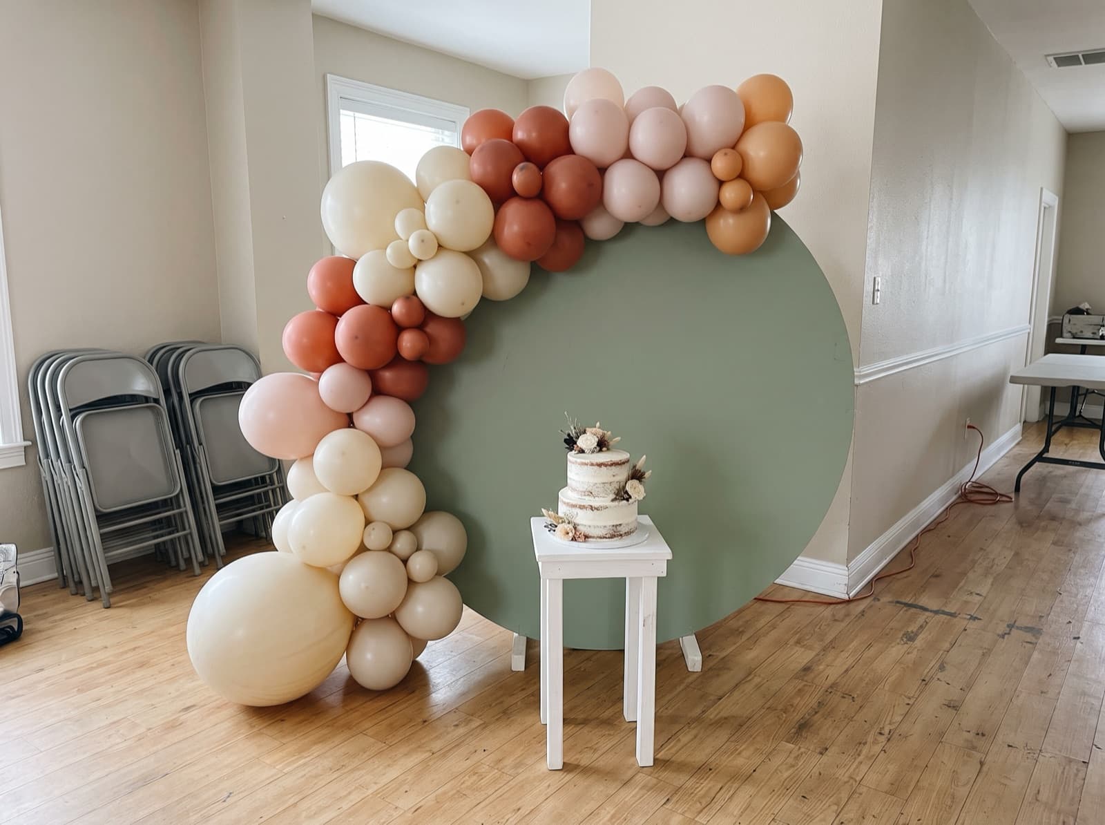 Round sage backdrop with a cream and terracotta balloon garland and a cake on a pedestal at an Austin birthday party