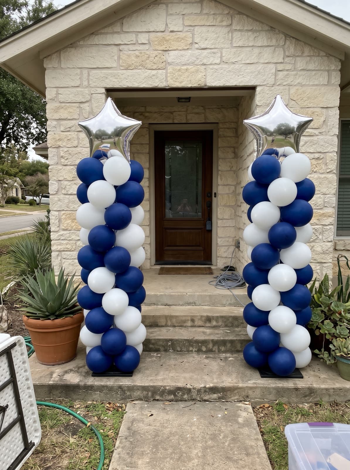 Two spiral balloon columns in navy and silver with silver star toppers beside the front door of an Austin limestone house