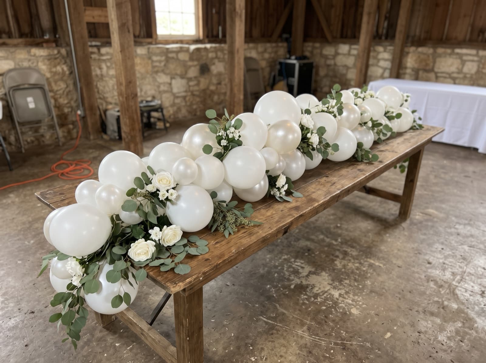 White and pearl balloon garland with eucalyptus on a farm table
