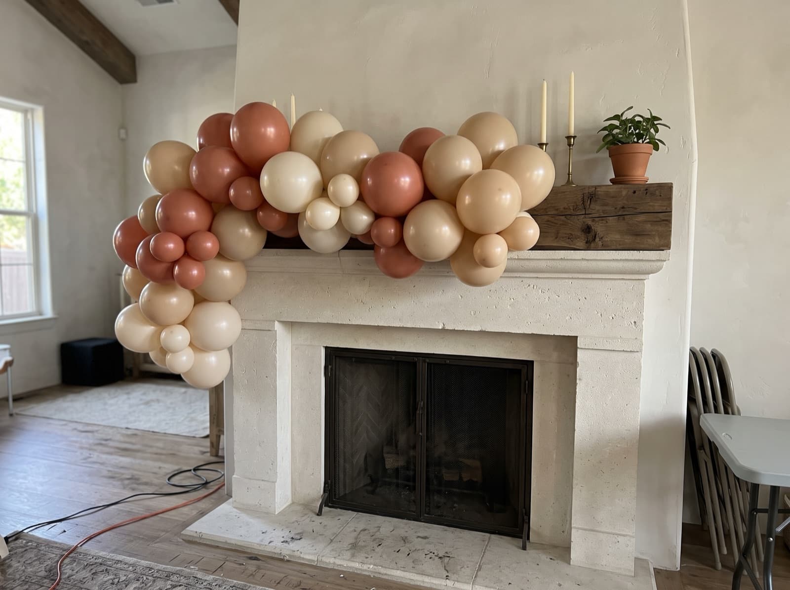 Organic balloon garland in terracotta, sand and cream along a limestone fireplace mantel in an Austin living room